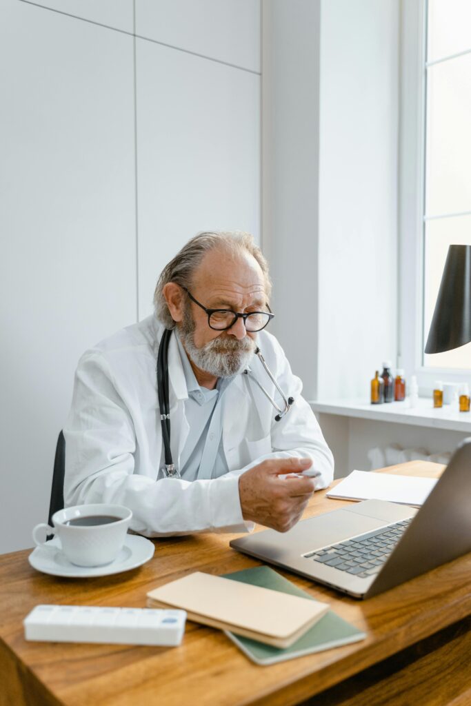 Elderly doctor using laptop for a virtual consultation in a modern office.
